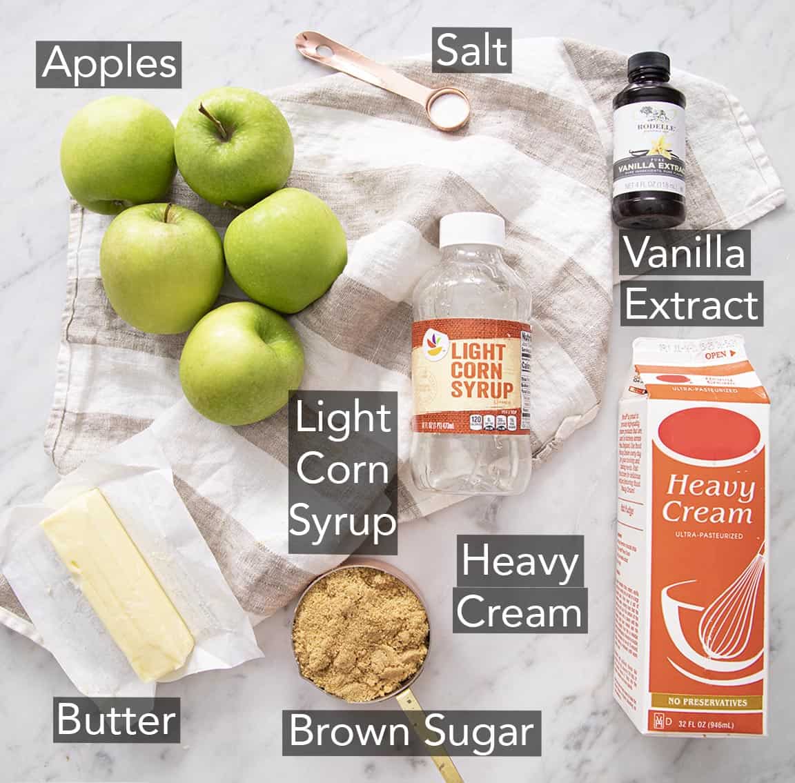 Ingredients to make caramel apples on a marble counter.
