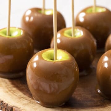 A group of caramel apples on a wooden plate.
