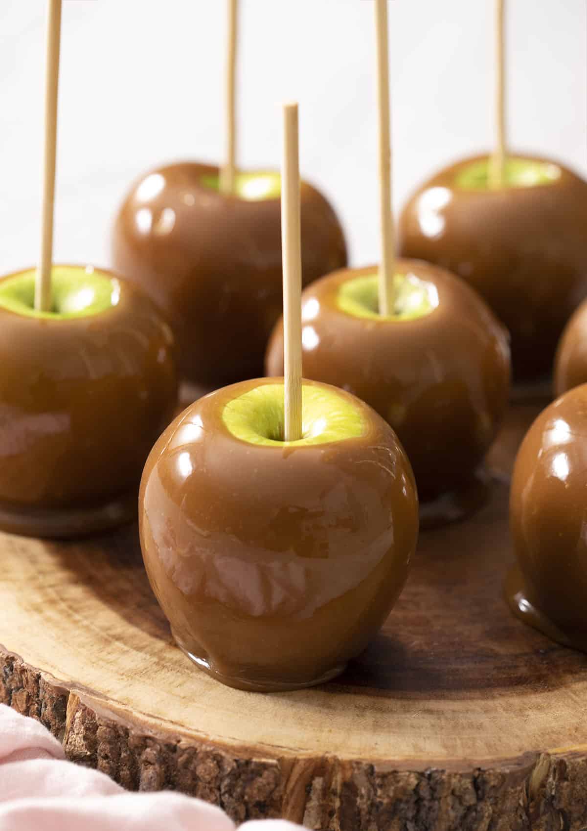 A group of caramel apples on a wooden plate.