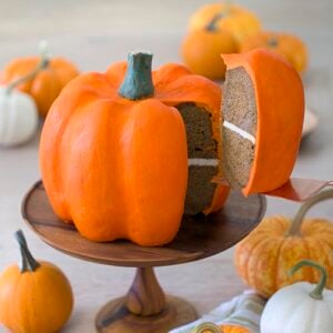 photo of a pumpkin shaped cake on a wooden stand with a piece being removed.