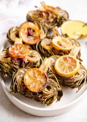 A side shot of roasted artichokes on a serving plate