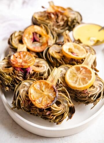 A side shot of roasted artichokes on a serving plate