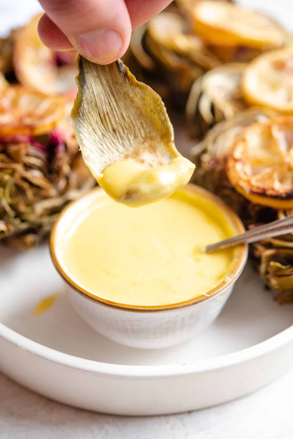 A close up of dipping an artichoke leave into aioli