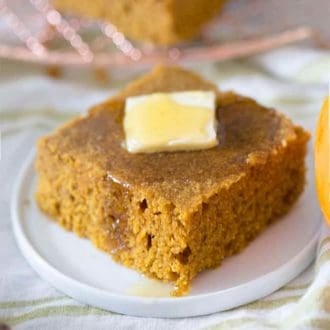 A piece of pumpkin cornbread on a small white plate with butter on top