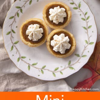 Three mini pumpkin pies with whipped cream on a plate.