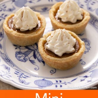 Three mini pumpkin pies topped with whipped cream on a small plate.