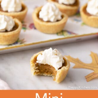 A group of mini pumpkin pies, the one in the foreground has a bite taken out.