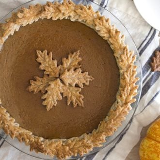 Photo of a pumpkin pie with pastry leaves on a blue and white linen.