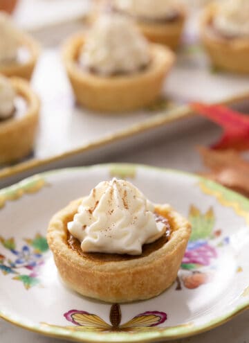 Mini pumpkin pies topped with whipped cream on a marble counter.
