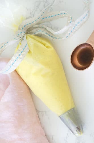 A photo of pastry cream in a piping bag with a tablespoon of vanilla extract next to it.