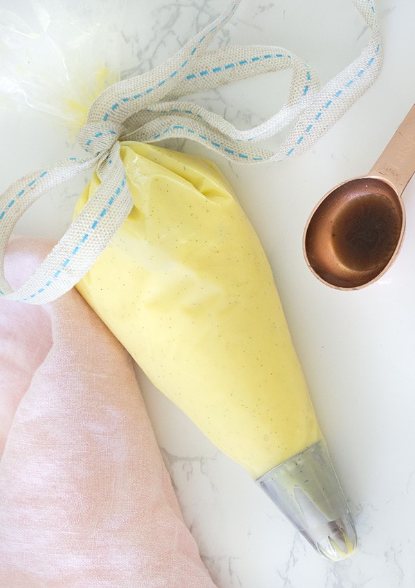 A photo of pastry cream in a piping bag with a tablespoon of vanilla extract next to it.