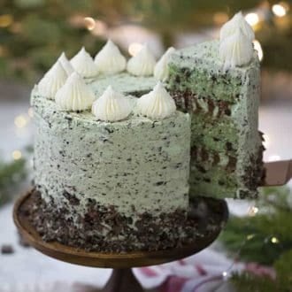 A mint chip cake on a wooden cake stand with a piece being removed