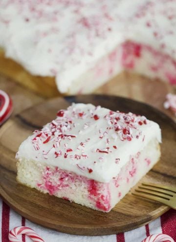 A photo showing a slice of Candy Cane Sheet Cake on a plate with crushed candy cane sprinkled on top.