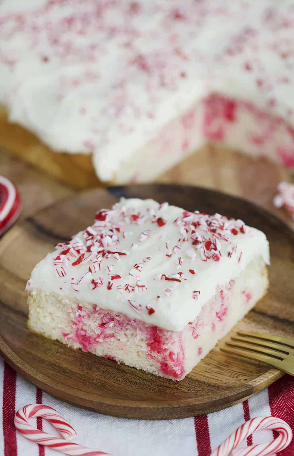 A photo showing a slice of Candy Cane Sheet Cake on a plate with crushed candy cane sprinkled on top.