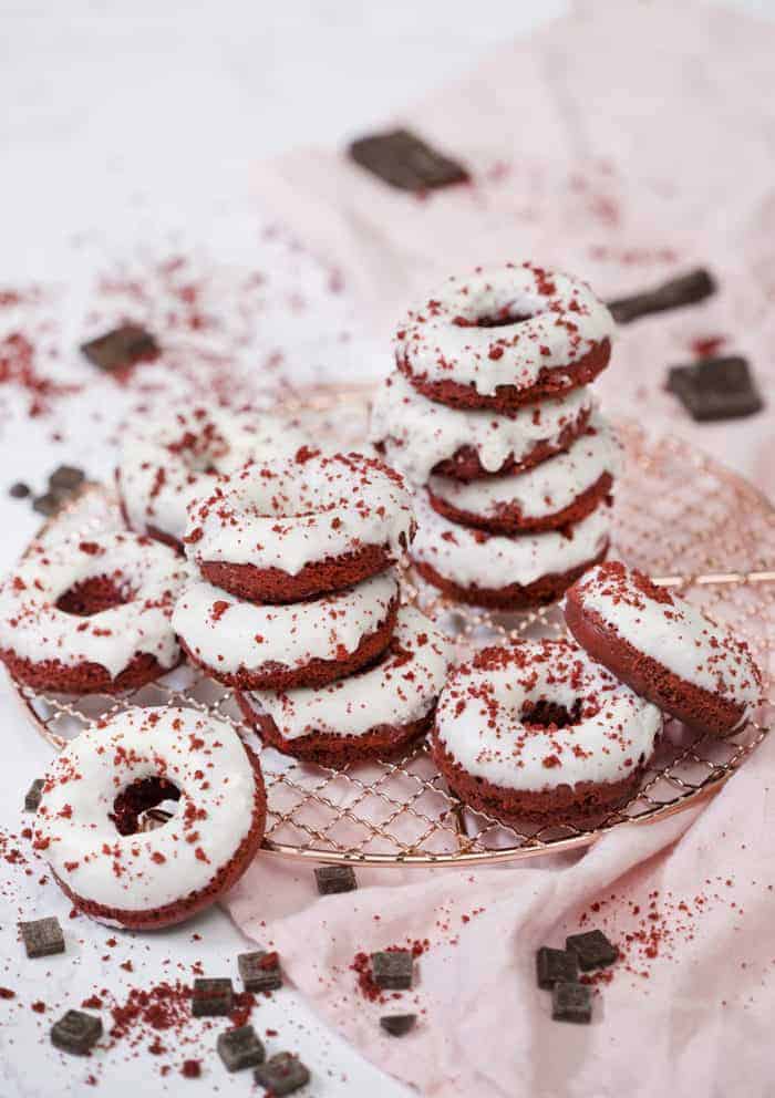 A photo of a group of Red Velvet Donuts on a copper cooling rack with a light pink linen underneath