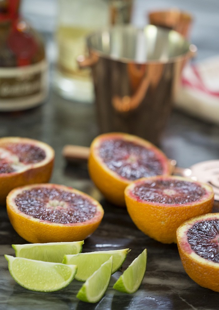 A photo showing cut blood oranges and limes on a black soapstone counter