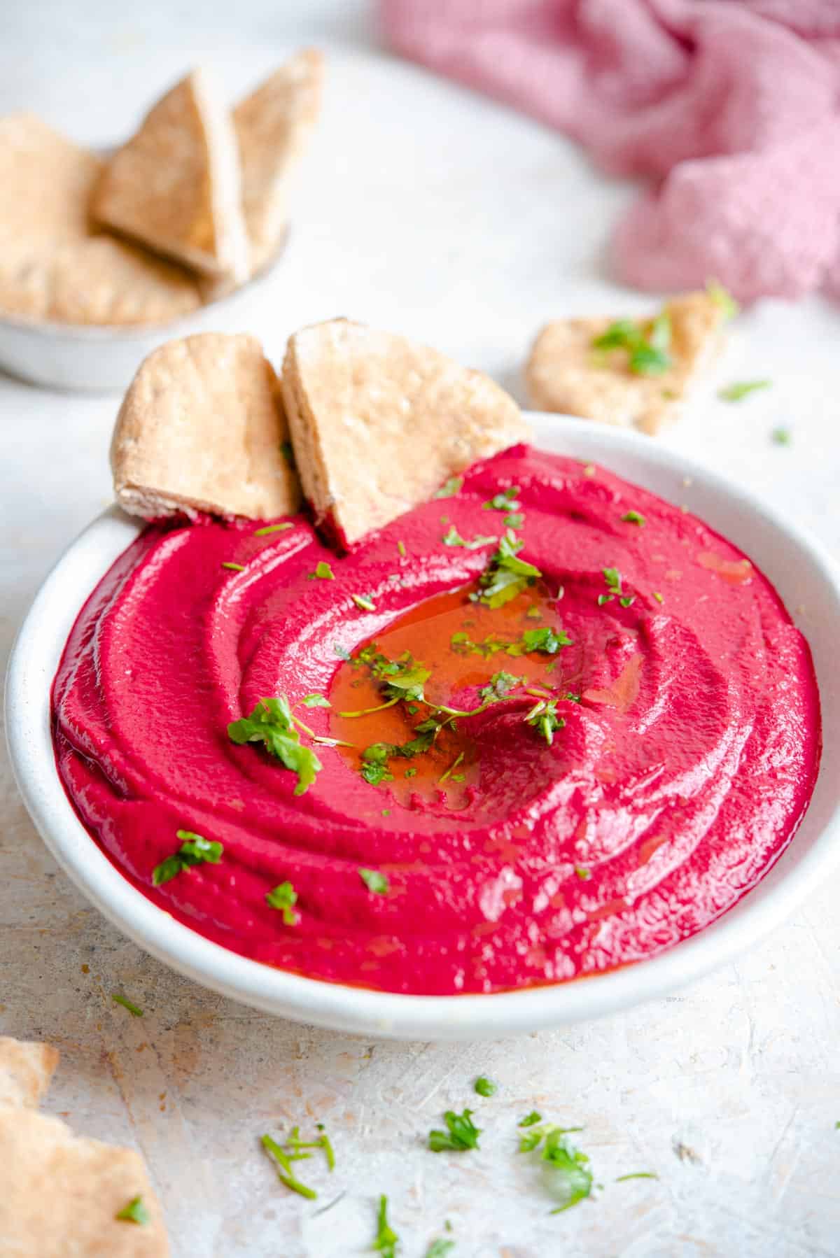 A side shot of beet hummus in a bowl with pitta bread at the side