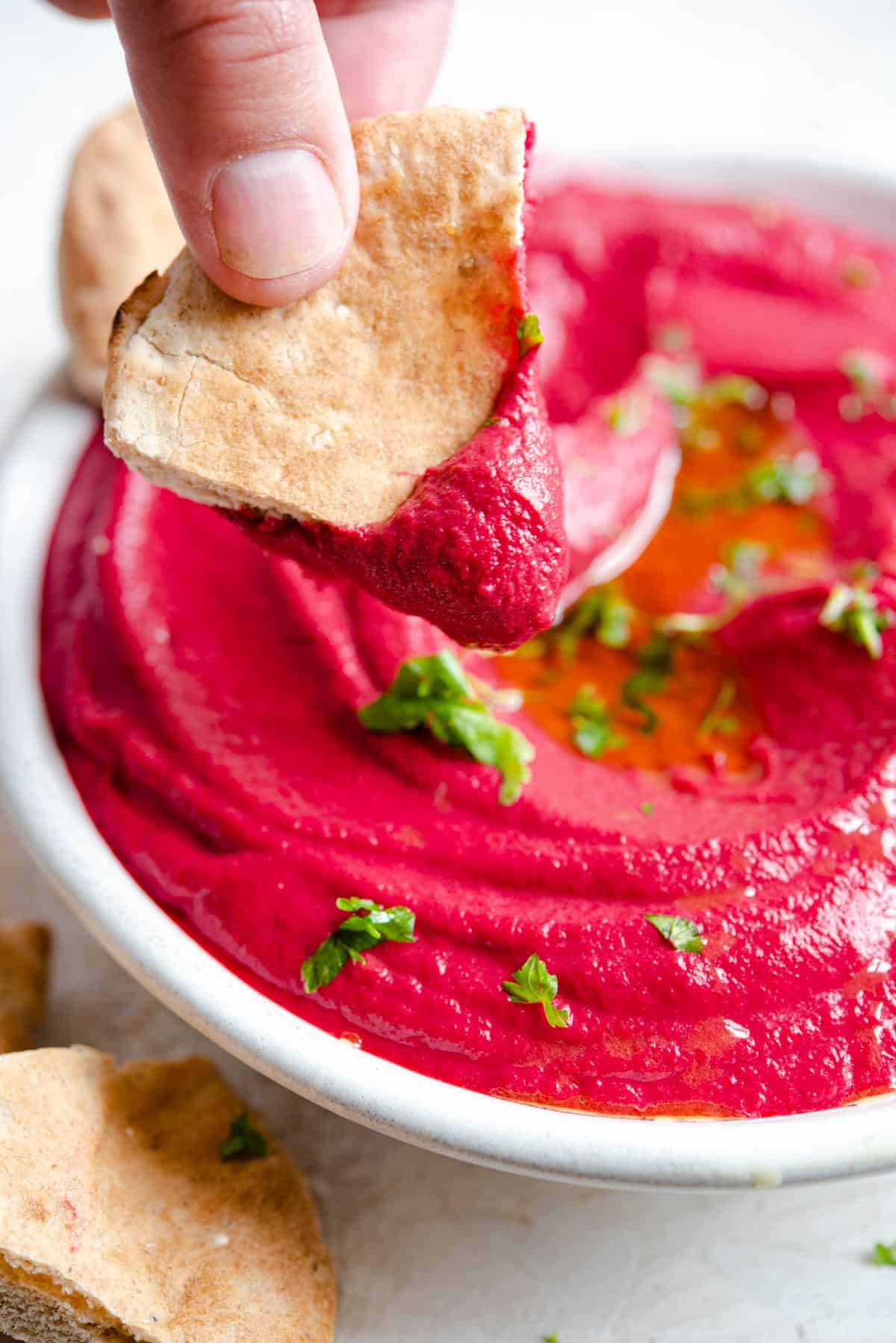 A close up of pitta bread dipping into beetroot hummus