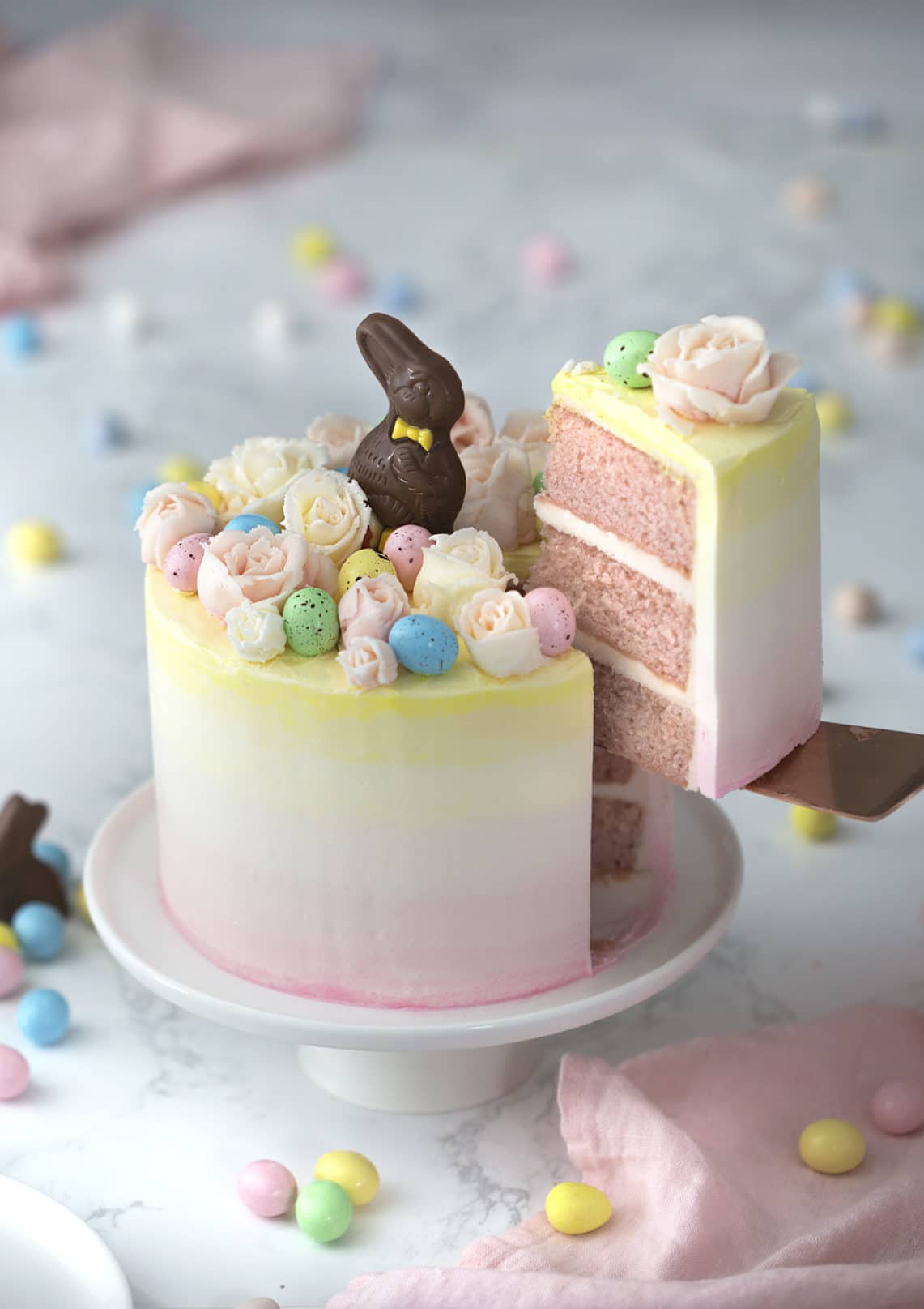 A photo of an Easter bunny cake with buttercream flowers, chocolate eggs and a chocolate Easter bunny on top.