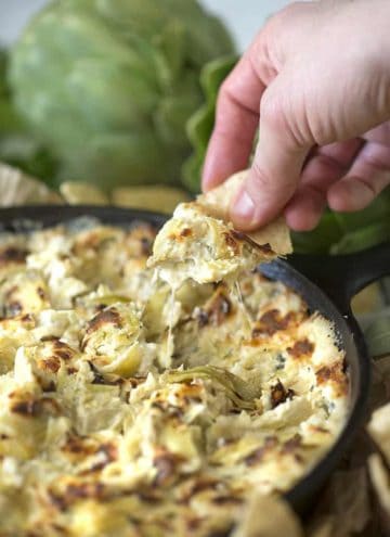 Artichoke dip in a skillet with a chip coming out.