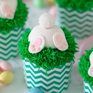 Three bunny butt cupcakes with mini chocolate eggs on the side.