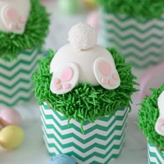 Three bunny butt cupcakes with mini chocolate eggs on the side.