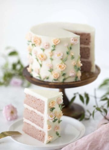Photo of a strawberry cake on a wooden cake stand covered in buttercream roses with a piece out