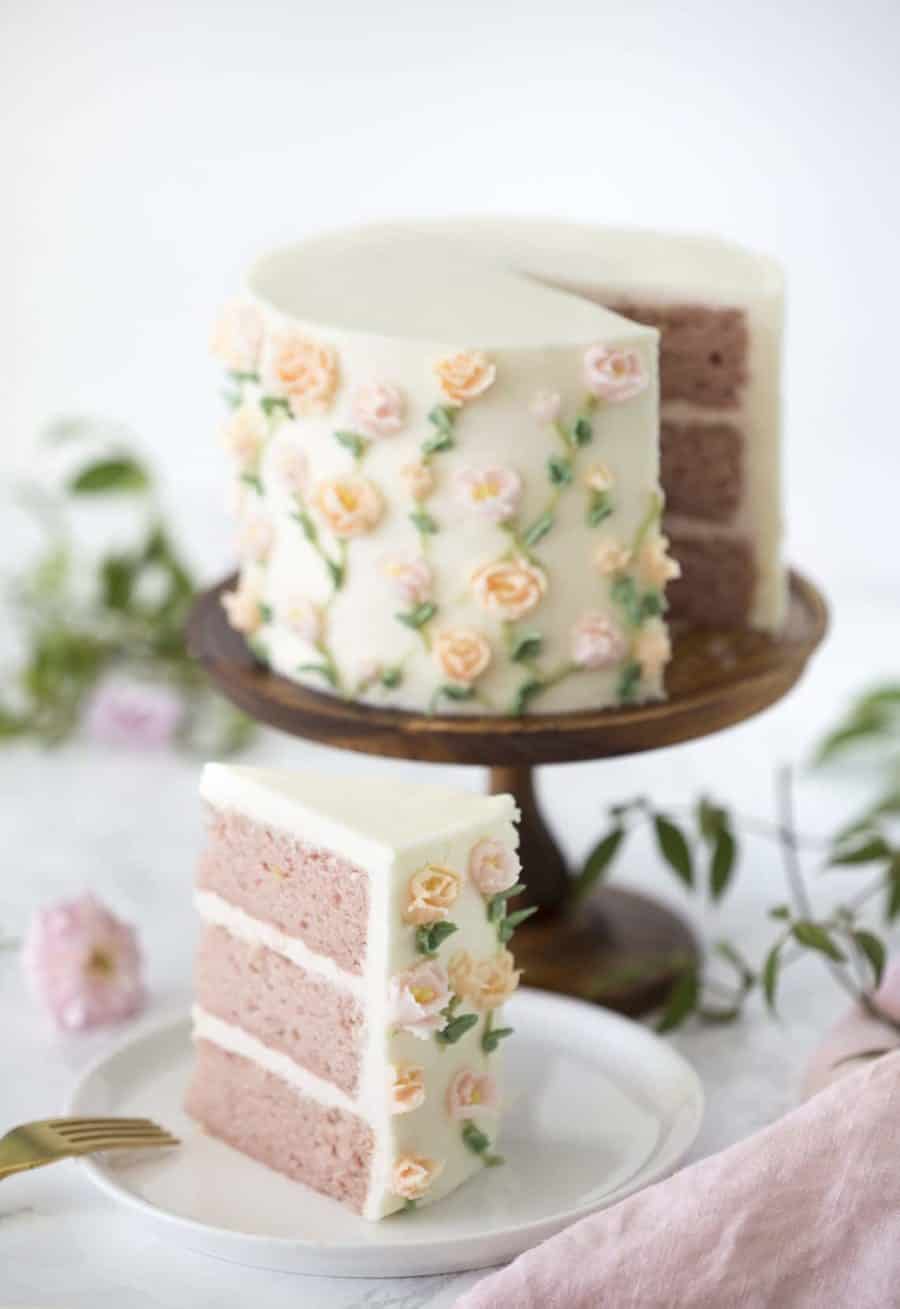 Photo of a strawberry cake on a wooden cake stand covered in buttercream roses with a piece out