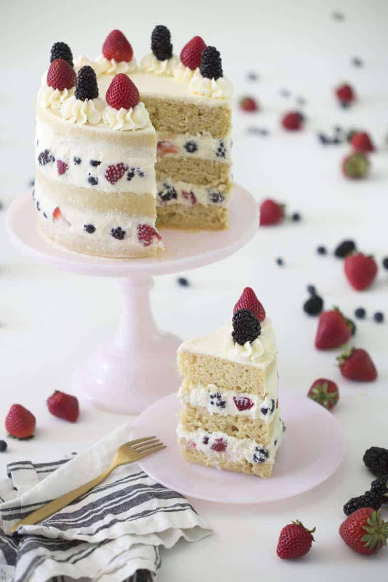 Photo of a Berry Cake cake on a pink cake stand with a piece on a plate