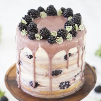 A photo of a blackberry cake with a soft purple blackberry drizzle and a crown of fresh blackberries.