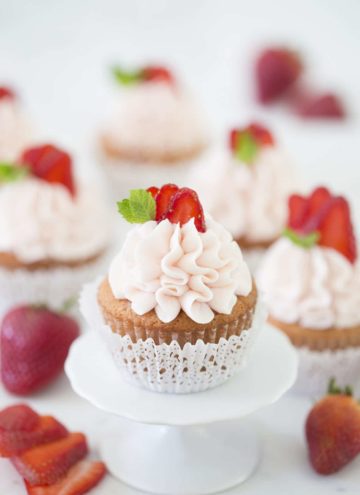 Photo of a group of Strawberry cupcakes in lace-like paper wrappers on a white marble table