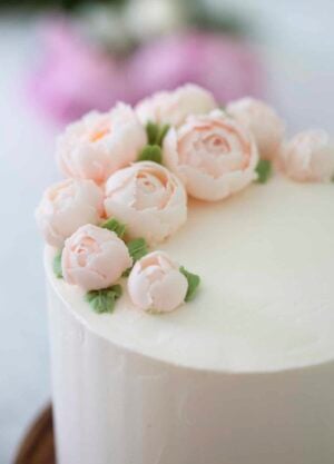 Close up 3/4 view of a lemon elderflower cake topped with soft pink buttercream peonies