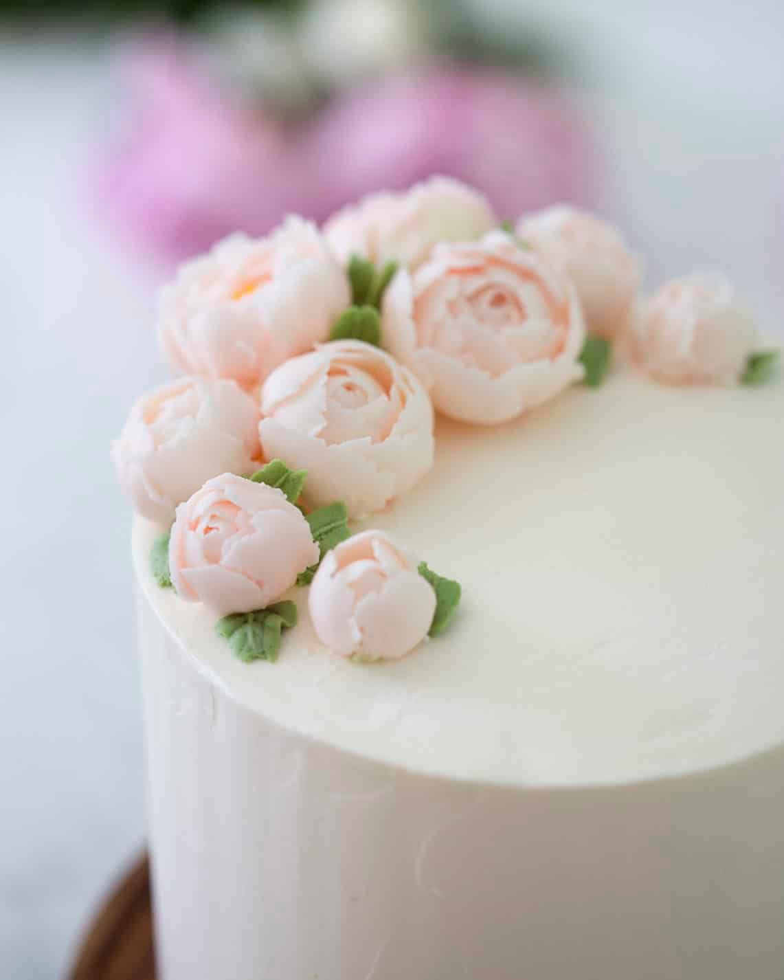 Close up 3/4 view of a lemon elderflower cake topped with soft pink buttercream peonies