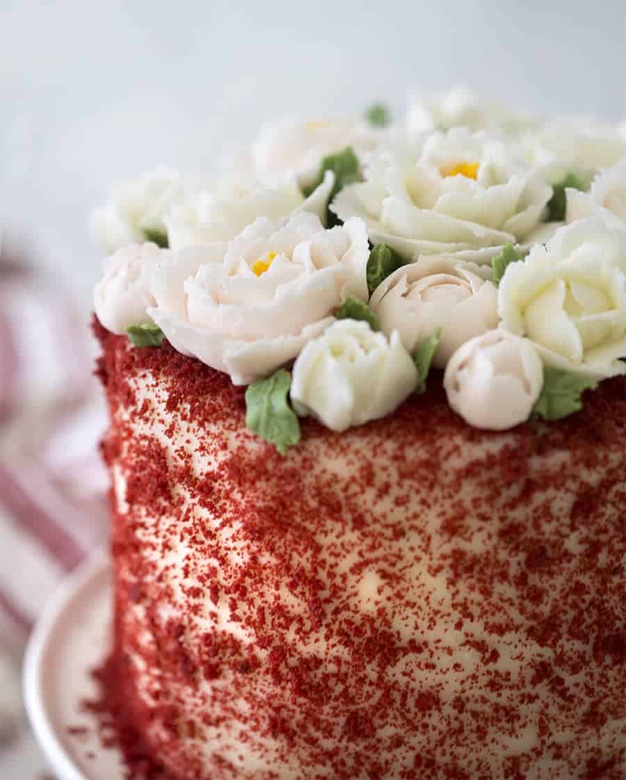 A close up shot of a Red Velvet Cake topped with soft pink and white buttercream roses