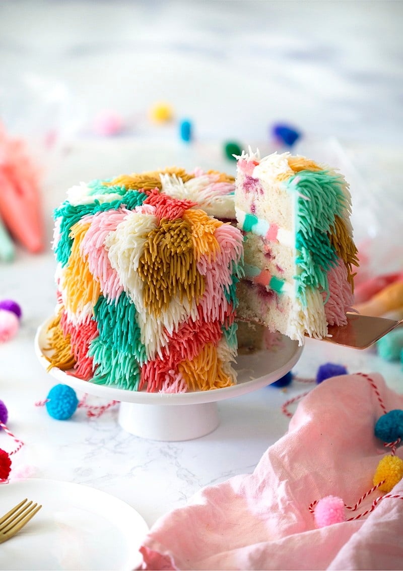 Photo of a colorful cake shag on a white cake stand with a piece being removed