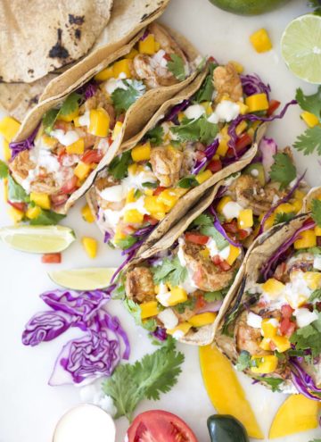 A photo of shrimp tacos topped with mango salsa, cabbage, cilantro and lime, taken from above.