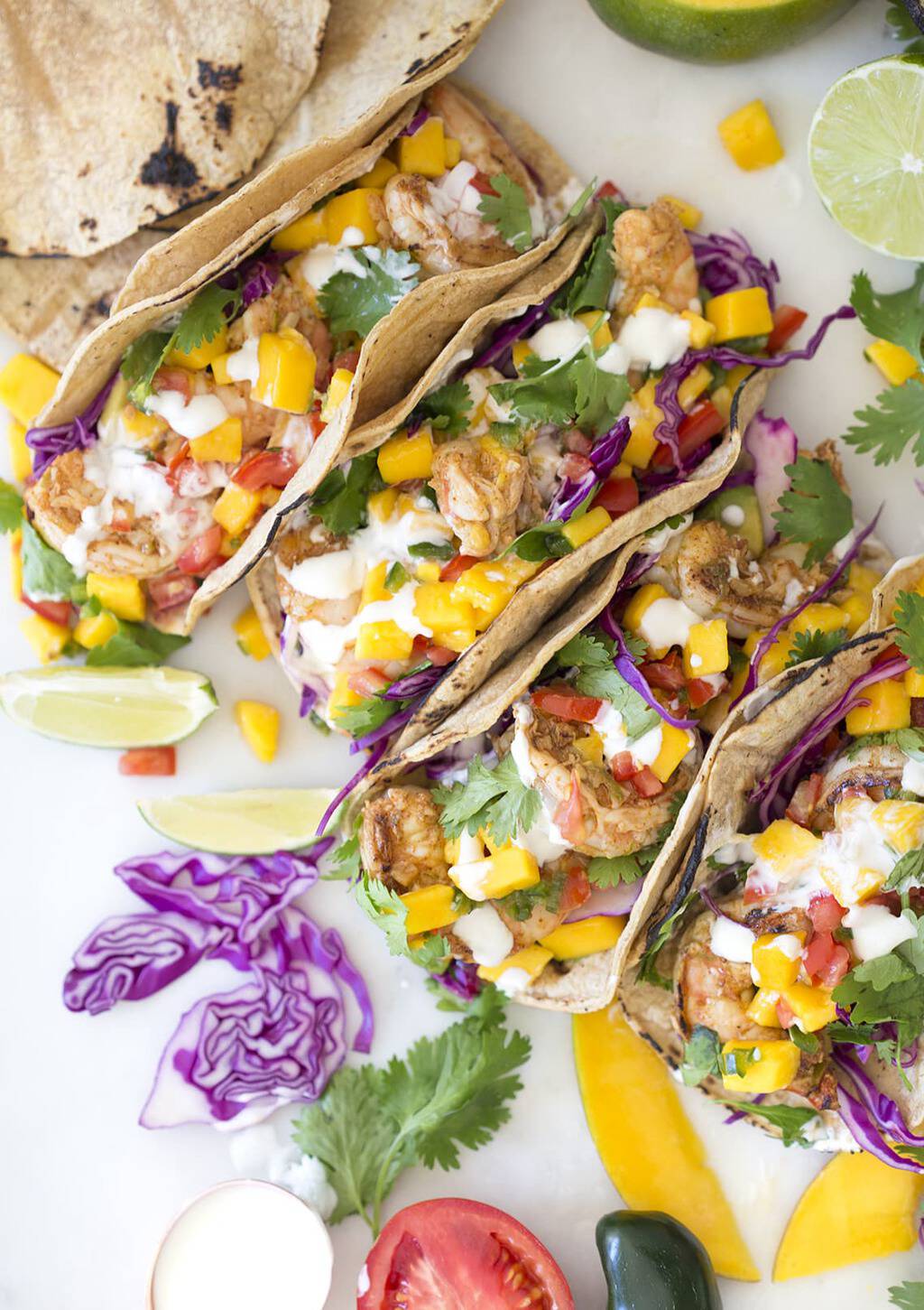 A photo of shrimp tacos topped with mango salsa, cabbage, cilantro and lime, taken from above.