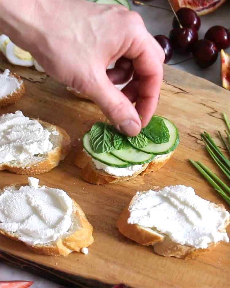 Cucumber slices and mint being added to make a canapé.