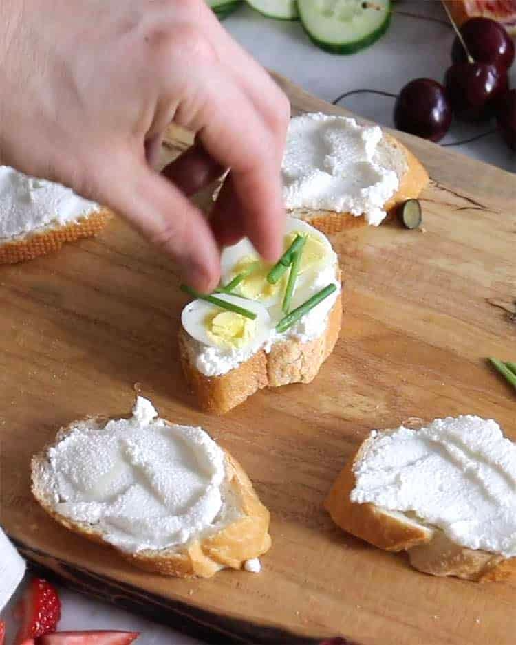 Hardboiled egg slices and chives being added to make a canapé.