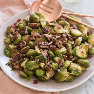 A photo of Brussel sprouts on a serving dish with crispy bacon and caramelized pecans.