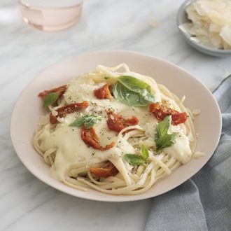 A photo of creamy Alfredo pasta with cheese, sun dried tomatoes and fresh basil on a plate.