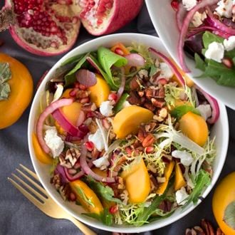Photo of a persimmon salad with pomegranate seeds and pecans in a white bowl