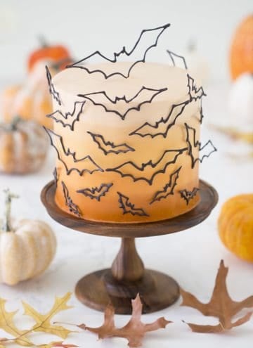 photo of an ombre orange cake covered in candy melt bats on a wooden cake stand