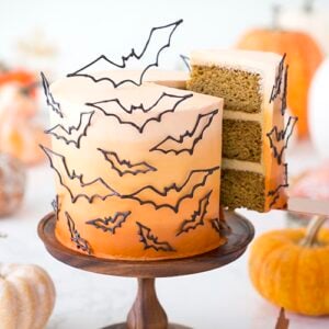photo of a n ombre orange cake covered in candy melt bats with a piece being removed.