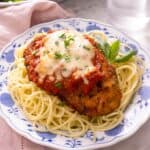 A close up of chicken parmesan on a plate on top of spaghetti