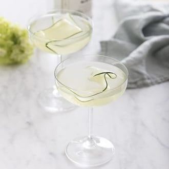 A photo of a cucumber martini in a coup glass on a white marble table