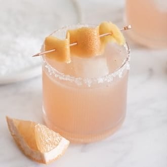 A photo of a soft pink paloma cocktail on a white marble table