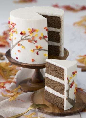 Photo of a spice cake on a wooden cak stand. A piece is removed and on a wooden plate in the foreground.