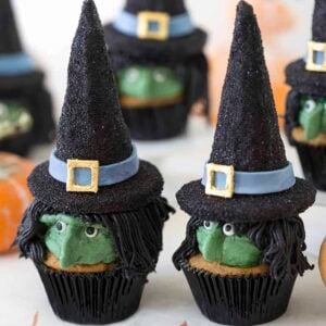 Two Halloween witch hat cupcakes with more cupcakes in the background.
