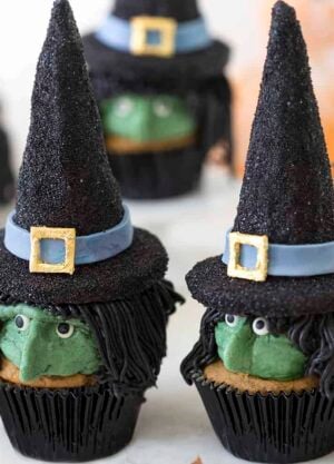 Two Halloween witch hat cupcakes with more cupcakes in the background.